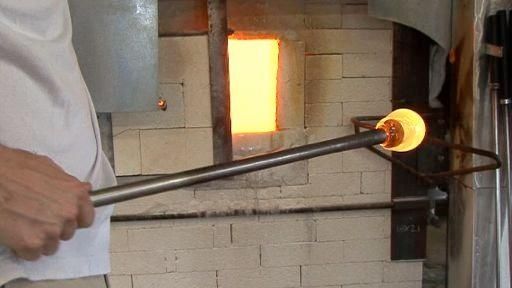 Artisan façonnant une boule de verre en fusion devant un four